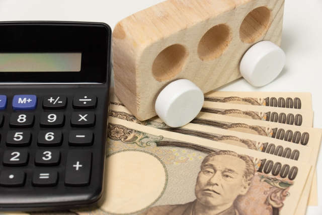 電卓と一万円札と木製の車のおもちゃ